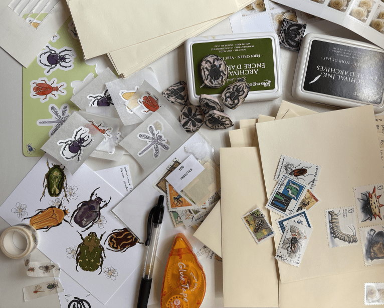 a pile of print club tools - letters, bug stamps for mail, rubber bug stamps, ink pads, washi tape, glue tape, stickers, prints, and a pen.